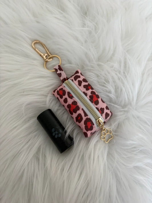 Distributeur de sacs à crottes fait main aux motifs léopard rouge et finitions dorées avec mousqueton et curseur patte de chat. Capacité : un rouleau de sacs à déjections canines, un rouleau de sacs offert