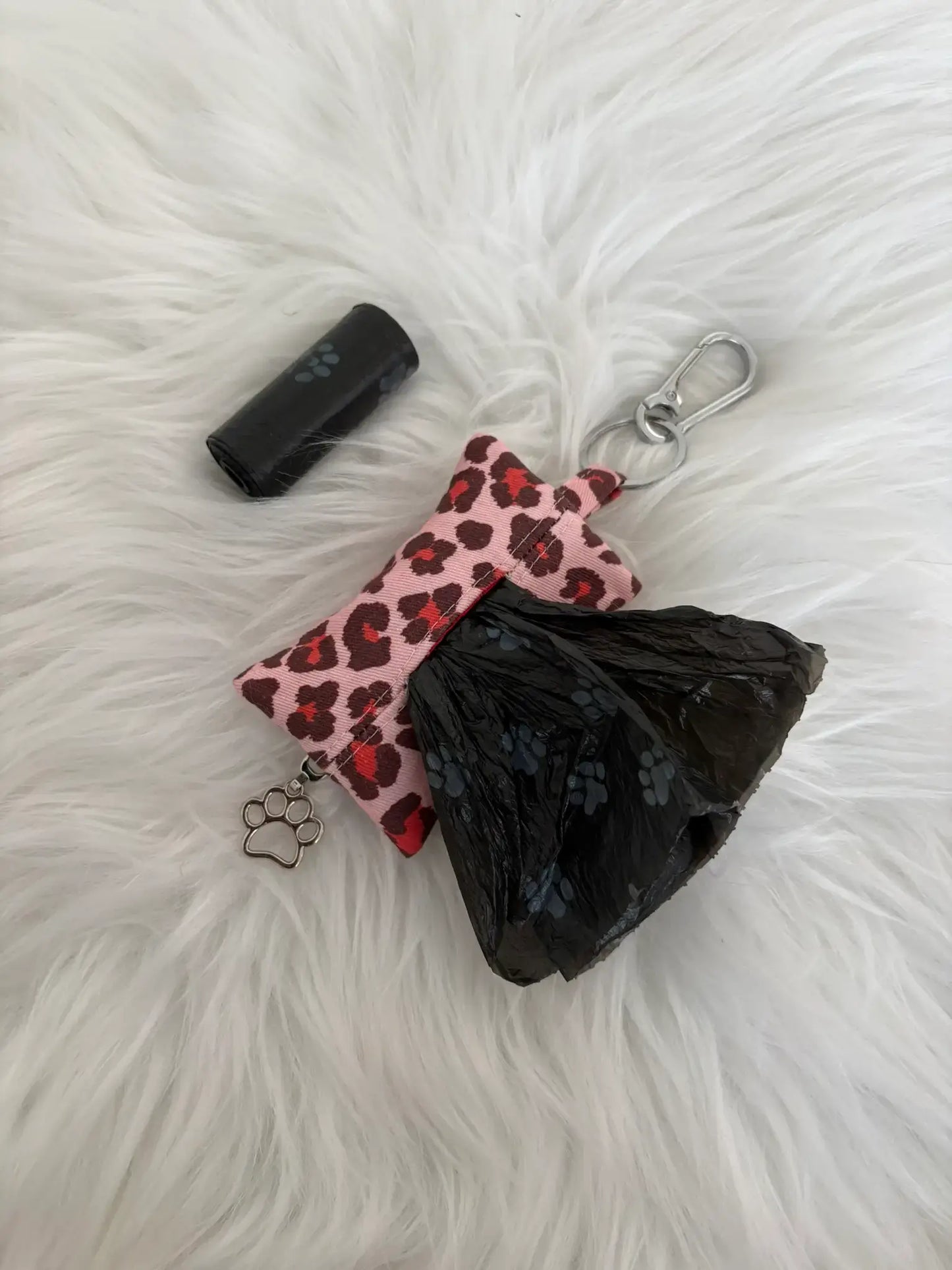 Distributeur de sacs à crottes fait main aux motifs léopard rouge et finitions argentées avec mousqueton et curseur patte de chat, vue de dos avec sacs intallés. Capacité : un rouleau de sacs à déjections canines, un rouleau de sacs offert