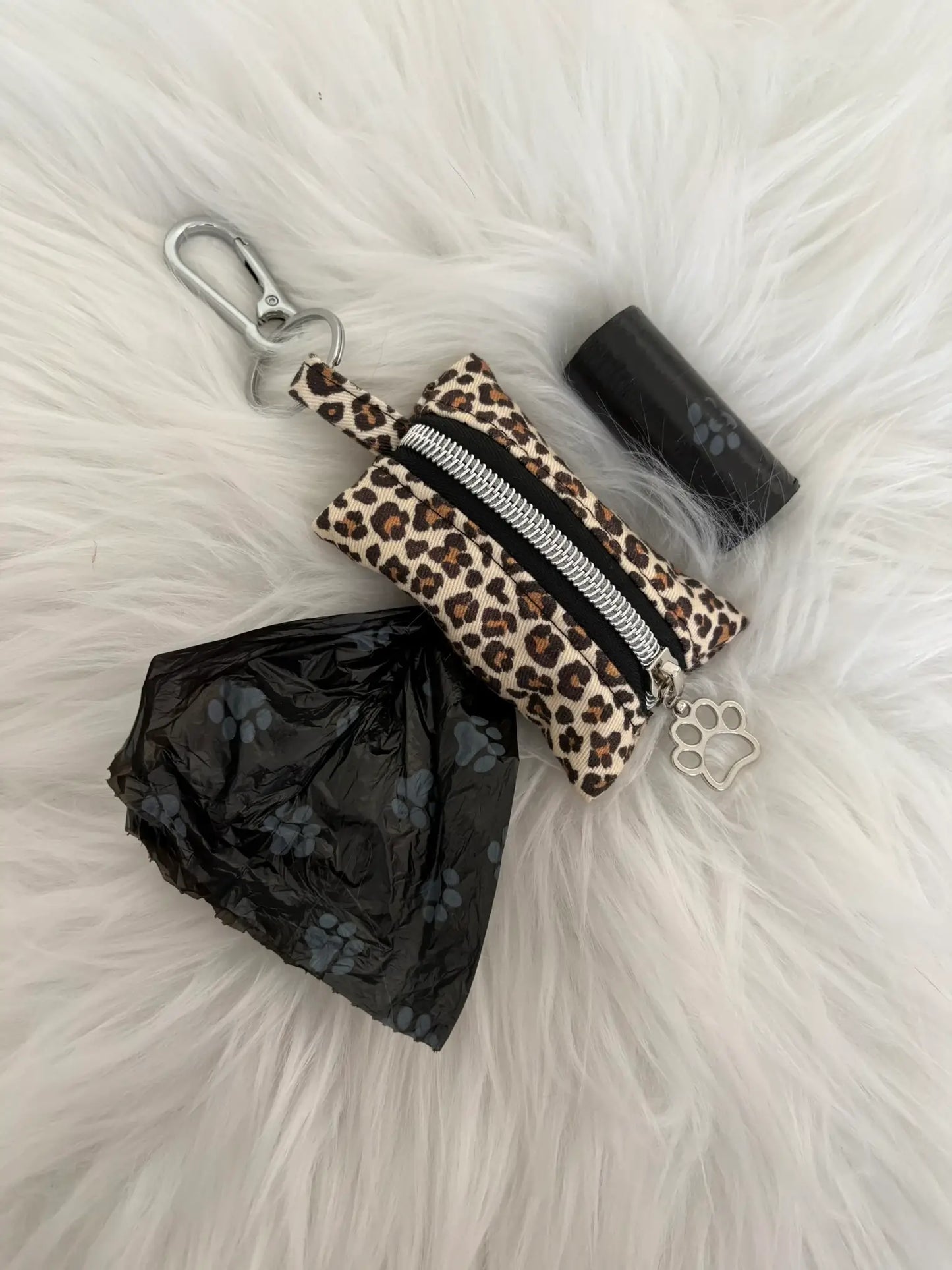 Distributeur de sacs à crottes fait main aux motifs léopard beige et finitions argentées avec mousqueton et curseur patte de chat, fermeture noire, vue de face avec sacs intallés. Capacité : un rouleau de sacs à déjections canines, un rouleau de sacs offert