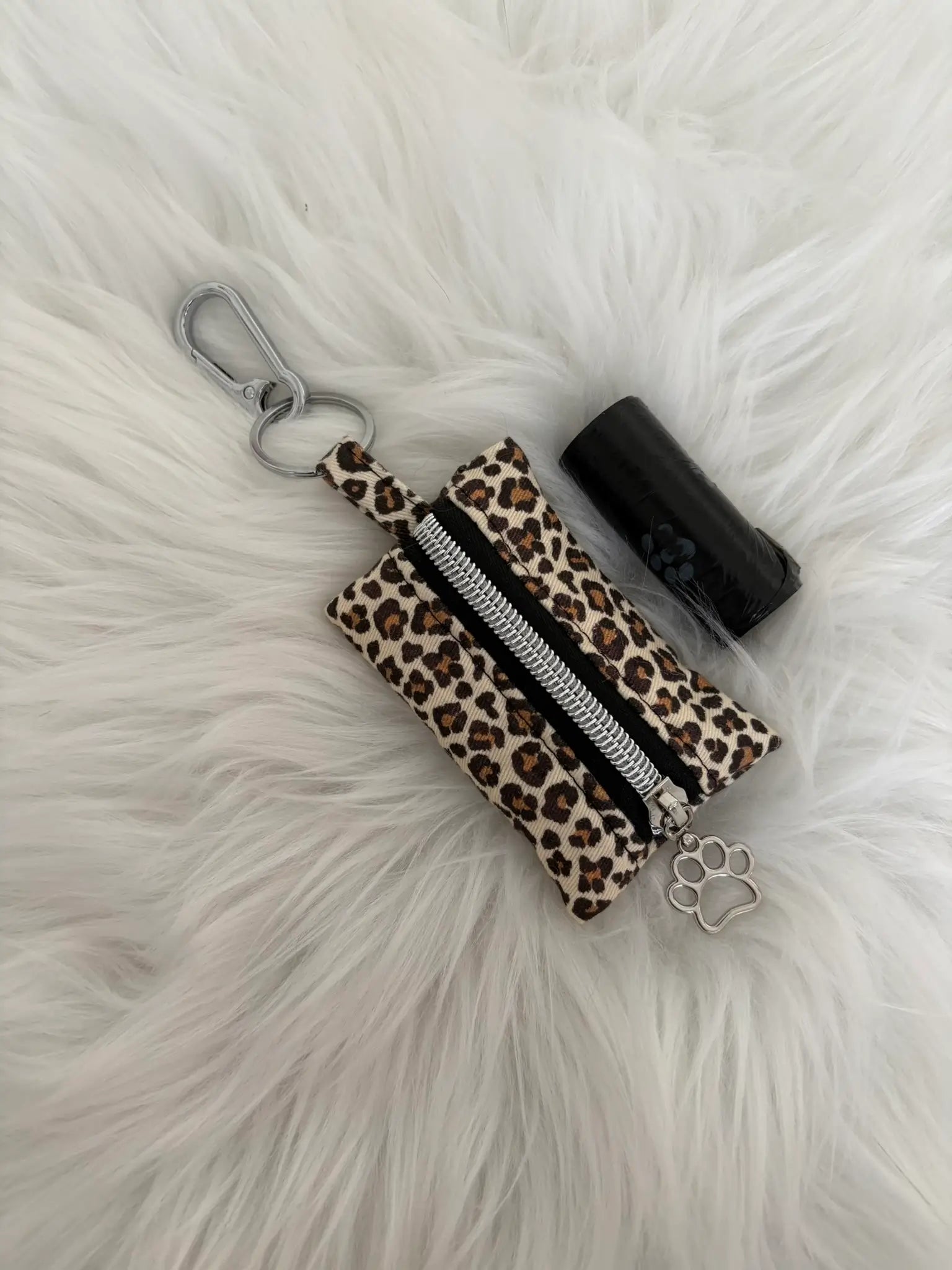 Distributeur de sacs à crottes fait main aux motifs léopard beige et finitions argentées avec mousqueton et curseur patte de chat, fermeture noire. Capacité : un rouleau de sacs à déjections canines, un rouleau de sacs offert