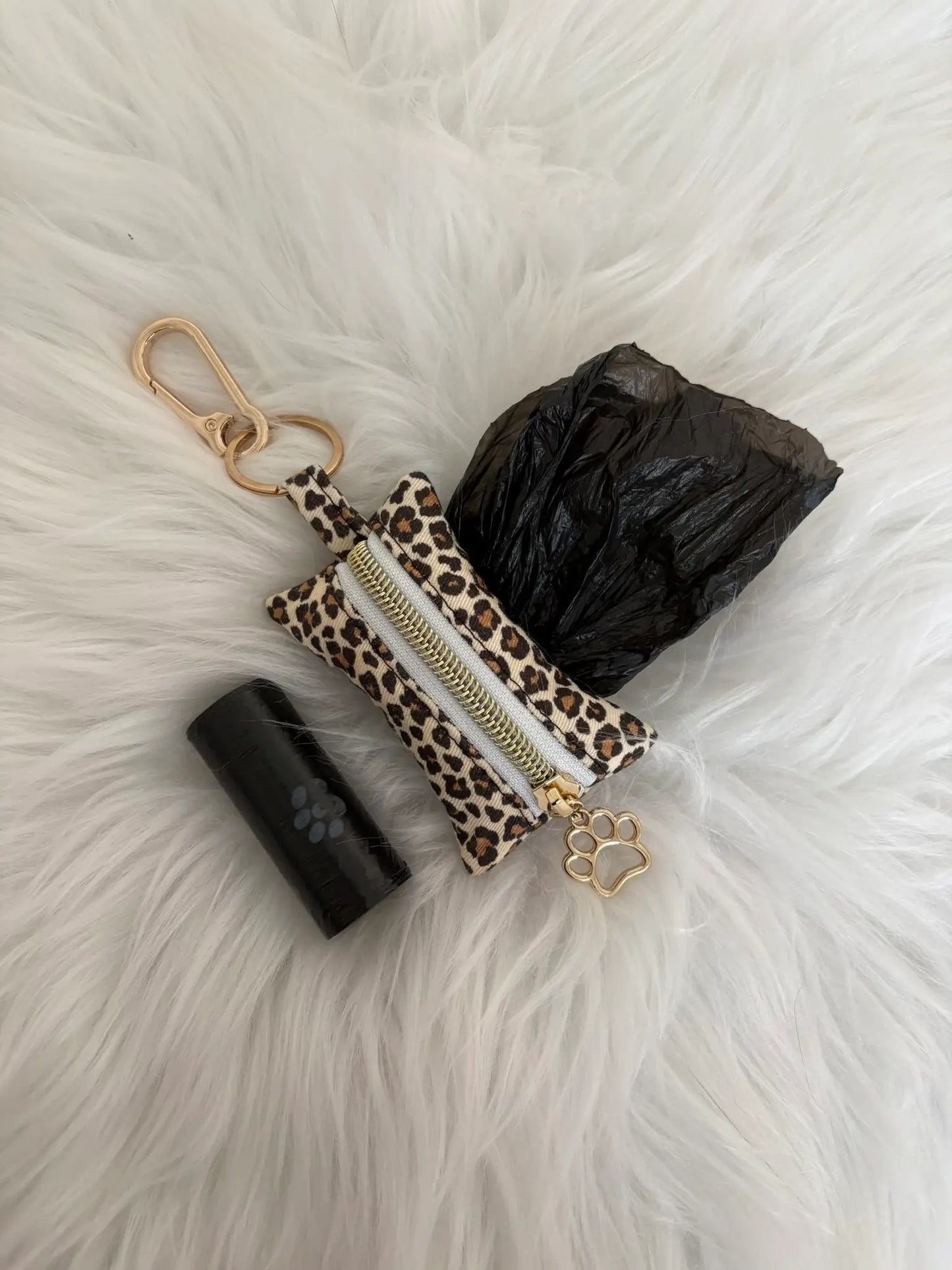 Distributeur de sacs à crottes fait main aux motifs léopard beige et finitions dorées avec mousqueton et curseur patte de chat, fermeture blanche, vue de face avec sacs intallés. Capacité : un rouleau de sacs à déjections canines, un rouleau de sacs offert